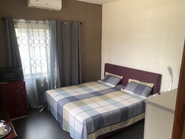 Une chambre à coucher avec un lit, des rideaux, une fenêtre et un four à micro-ondes.