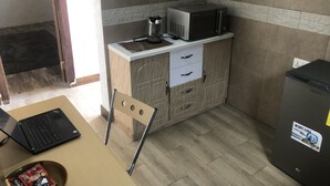 Een kleine keuken met een magnetron, koffiezetapparaat en een koelkast. Op een tafel staat een laptop en er is een stoel.