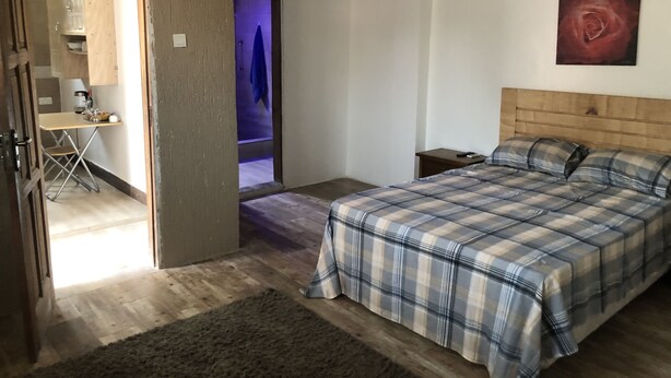 Een slaapkamer met een bed, nachtkastje, houten hoofdbord, schilderij en uitzicht op een andere kamer.