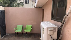 Een klein buitengebied met twee groene plastic stoelen, een witte airconditioning en een houten vloer.