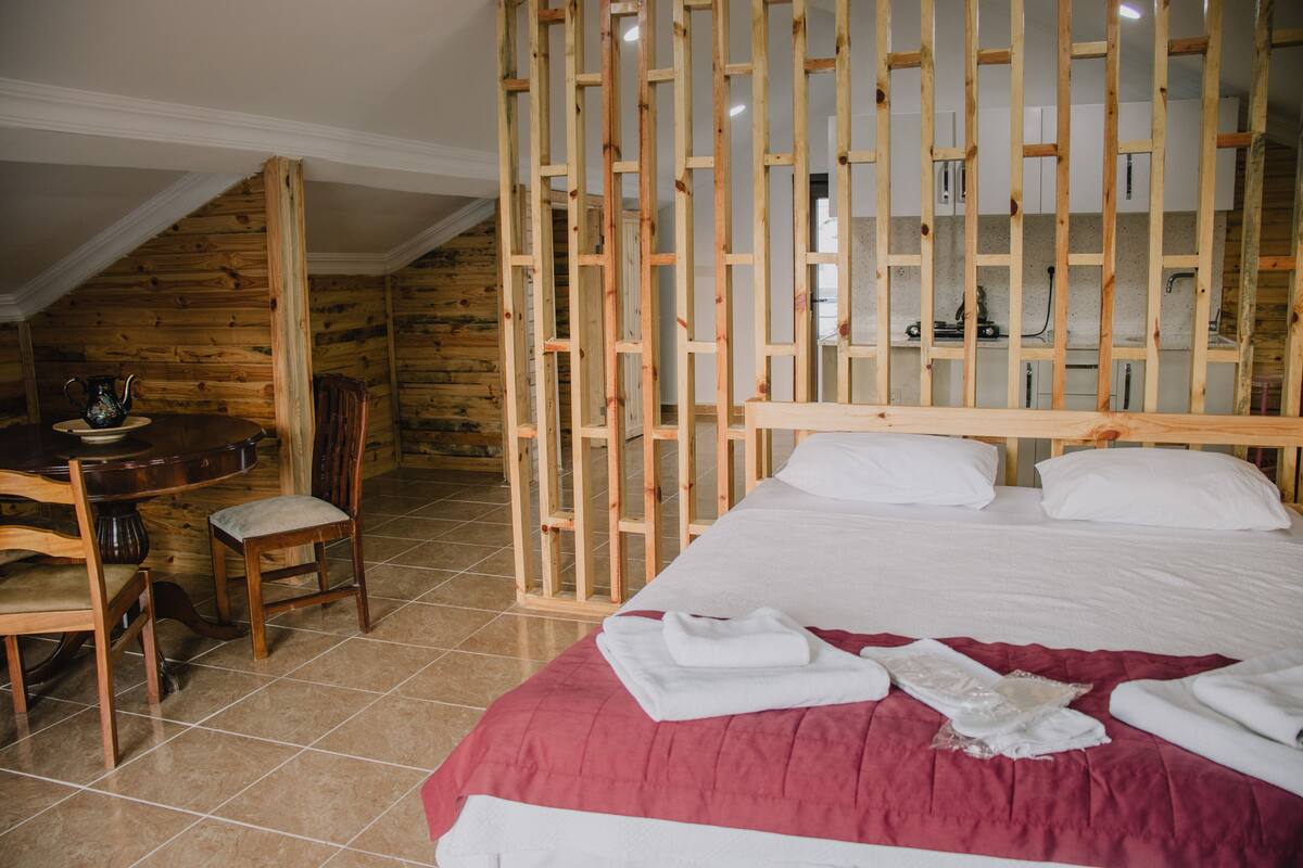 A bedroom with a wooden headboard, a bed with white linens, a red bedspread, and a wooden chair.