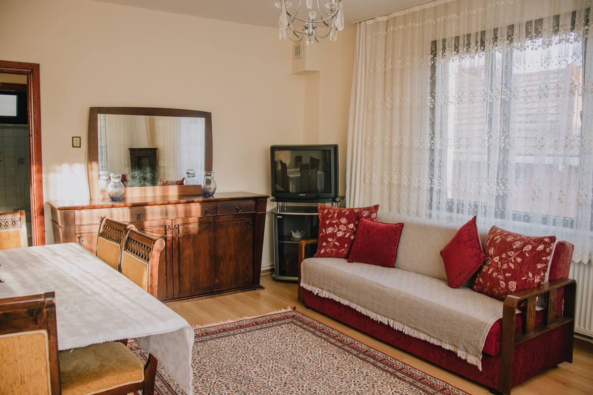 A living room with a sofa, a television, a dining table, and a chandelier.