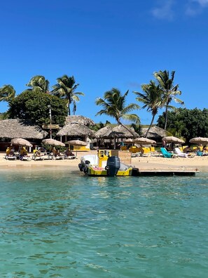 Una spiaggia con capanne a tetto di paglia, una barca e persone che si rilassano sulla sabbia.