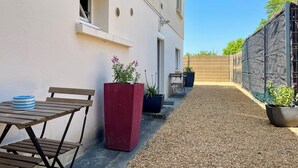 Een terras met een tafel en stoelen, potplanten en een grindpad.
