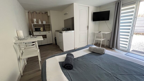 Een slaapkamer met een bed, bureau, stoel, televisie en een schuifpui.