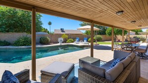 A covered outdoor area with a pool, lounge chairs, and a table with chairs. - HUGE, heated pool. Family friendly, toys for all!  Big & beautiful backyard!  (Mesa)