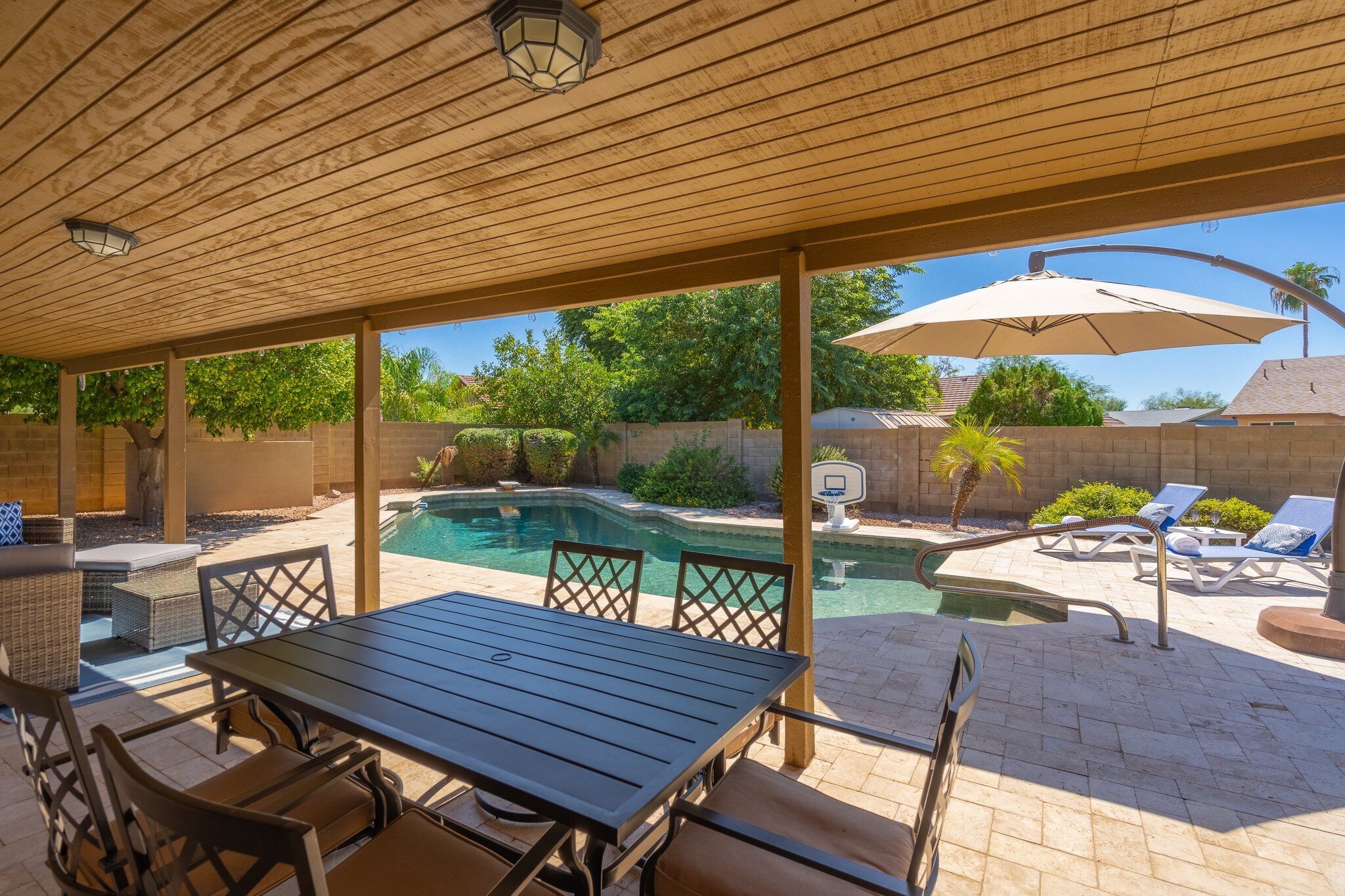 A covered patio with a pool, outdoor furniture, and a basketball hoop.