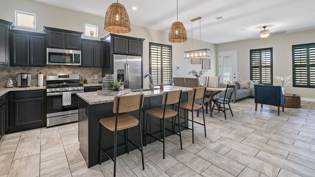 A modern kitchen with dark cabinetry, a central island with bar stools, and a dining area with a sofa and chairs. - Unique and Secluded home, traffic-free and quite (El Paso)