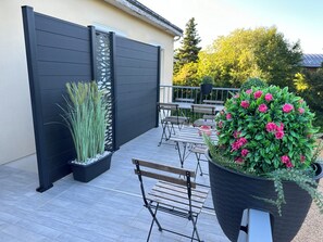 Eine Terrasse mit schwarzem Zaun, einer Holzbank und einem großen Pflanzgefäß mit rosa Blumen.