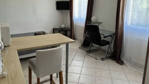 A modern room with a wooden table, a white chair, a black office chair, a TV on the wall, and a window with curtains. - The countryside, 5 minutes from downtown Tours (Fondettes)
