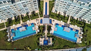 An aerial view of a modern hotel complex with two large swimming pools, a central courtyard, and surrounding greenery. - Villa Walking Distance to Eagle Beach (Noord)