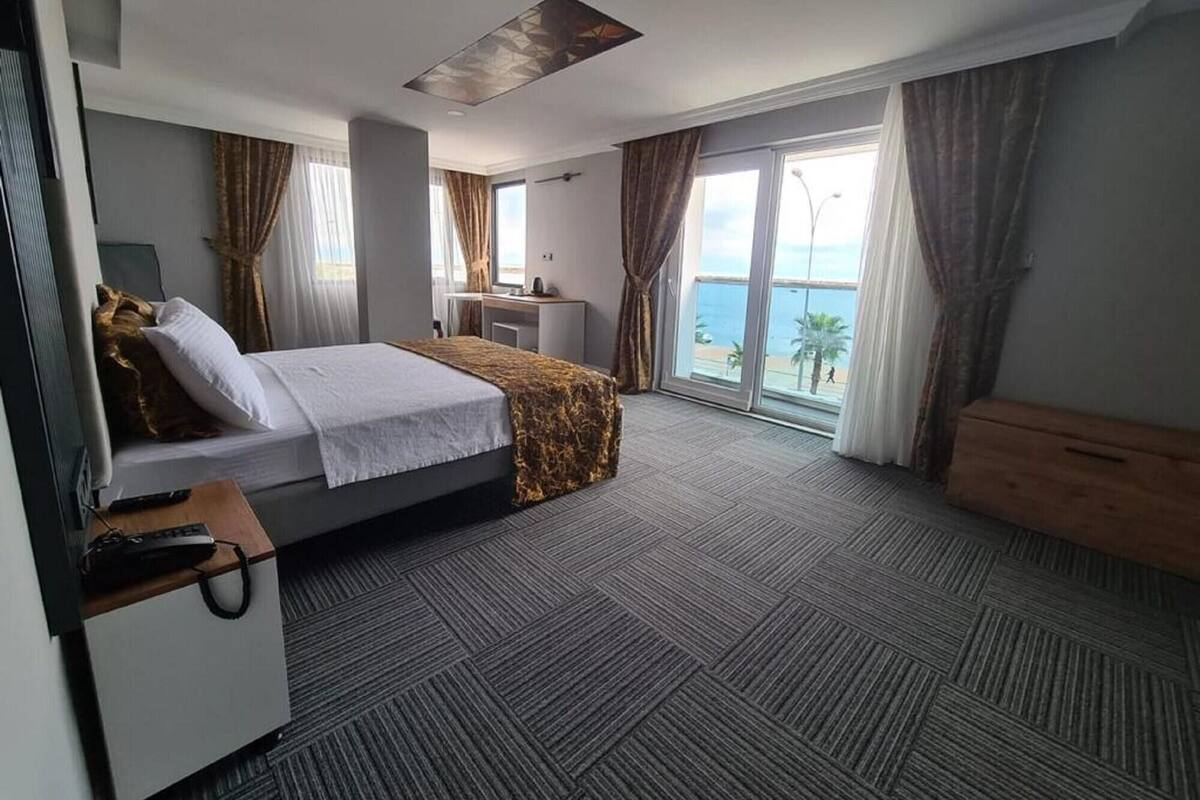 A hotel room with a bed, desk, and large windows with curtains.