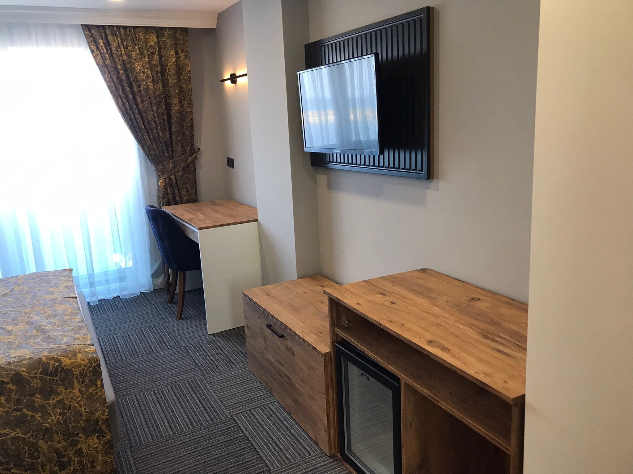 Une chambre d’hôtel avec un lit, un bureau, une chaise, une télévision et une fenêtre avec des rideaux.