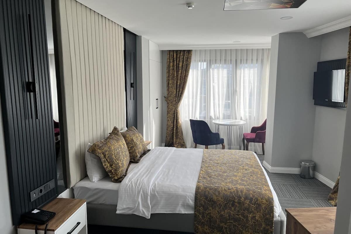 A hotel room with a bed, bedside table, chair, and a small desk.