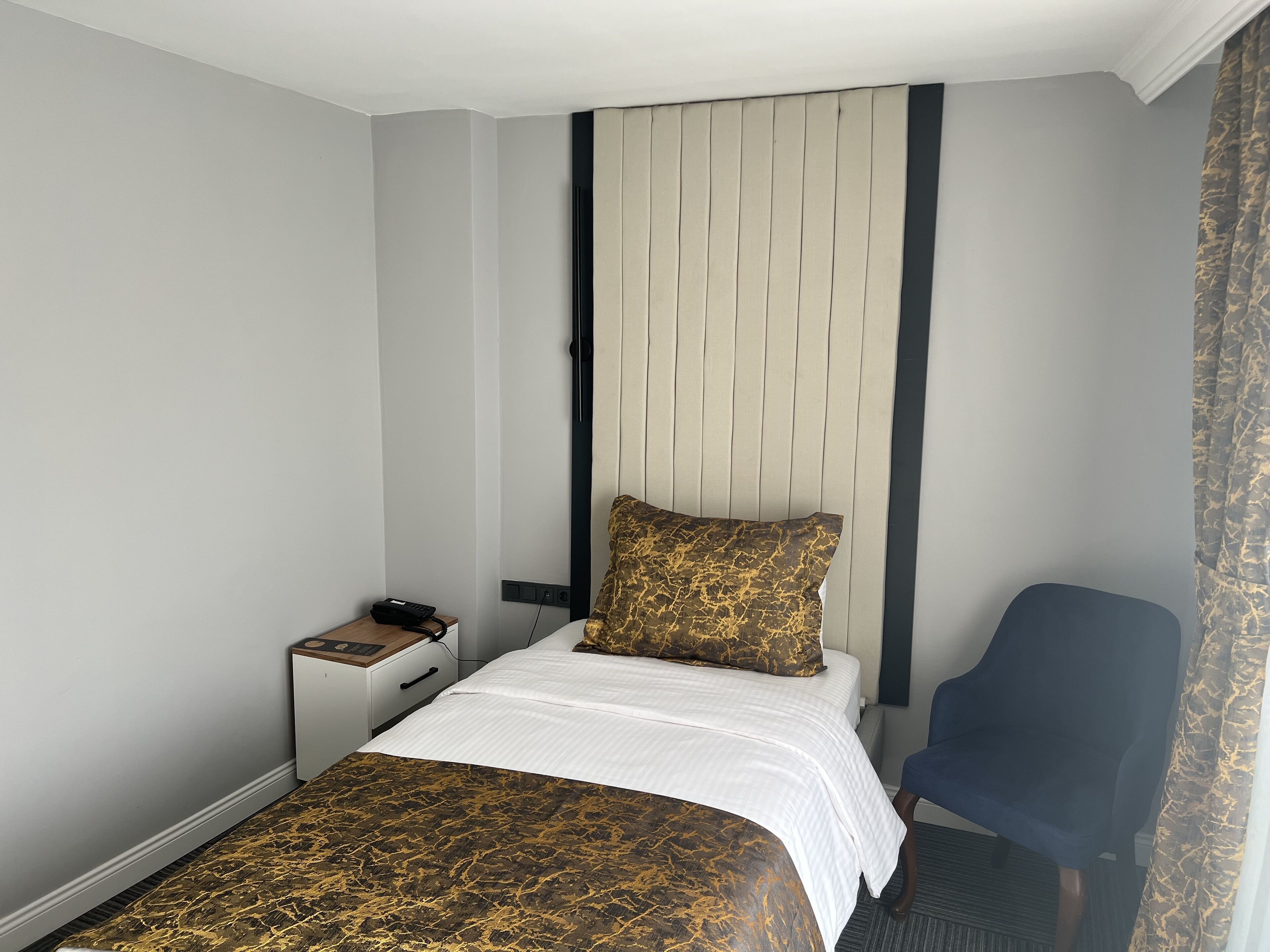 A hotel room with a bed, bedside table, chair, and a headboard with vertical slats.