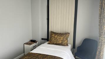 A hotel room with a bed, bedside table, chair, and a headboard with vertical slats.