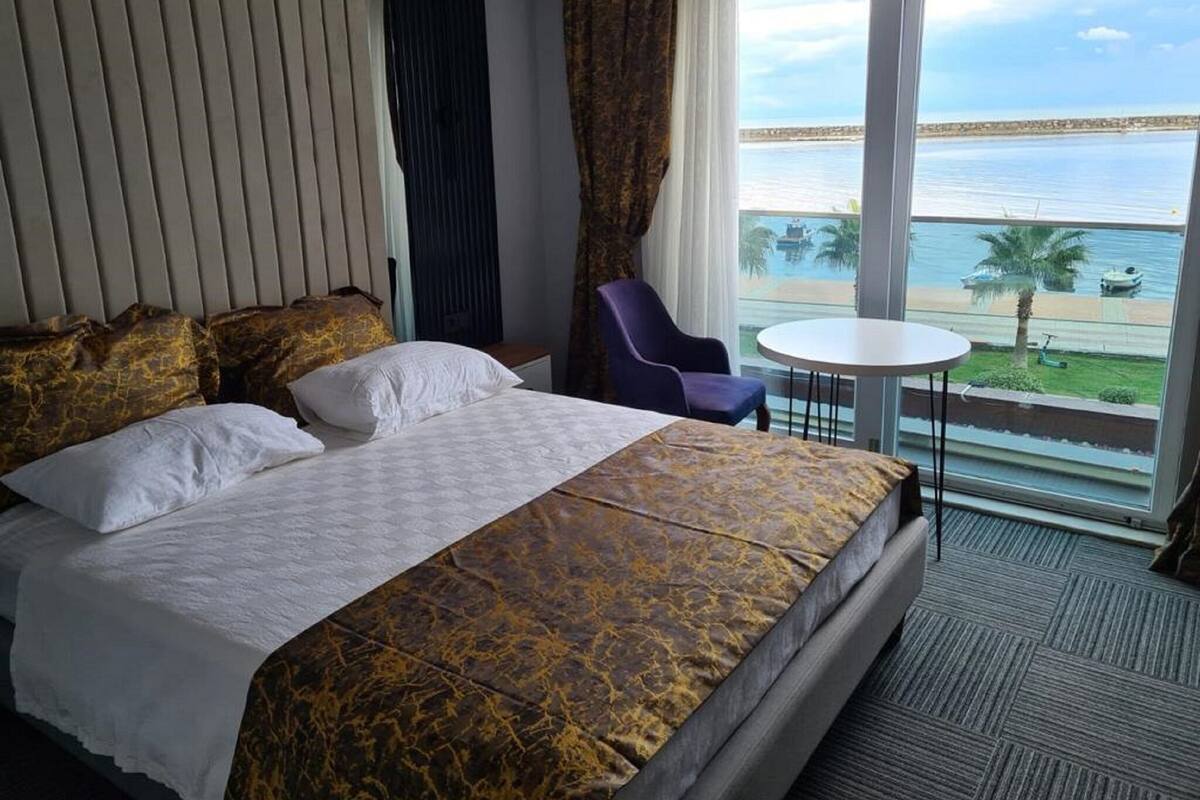 A hotel room with a bed, a chair, a small table, and a view of the sea.