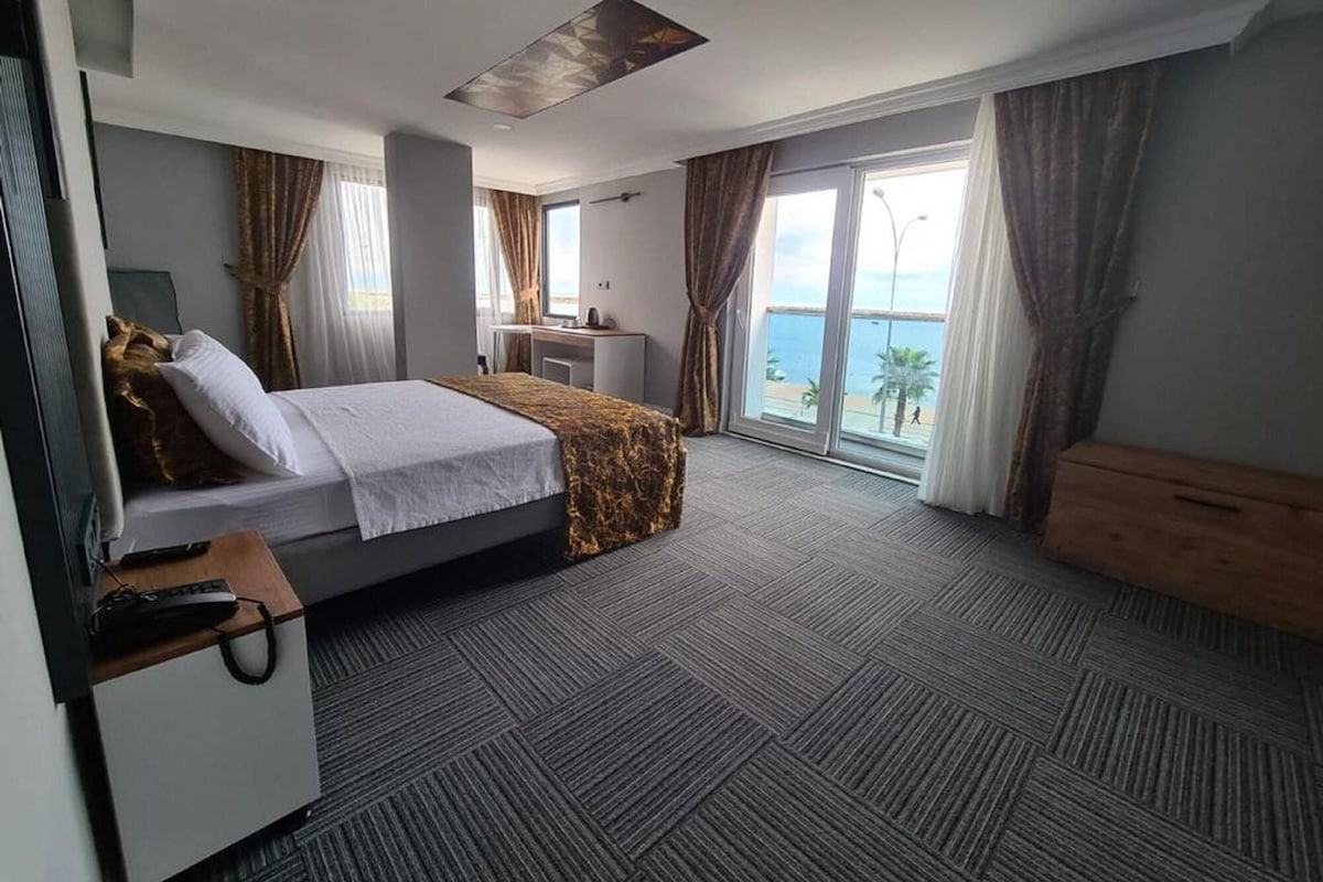Una habitación de hotel con cama, escritorio y ventanas grandes con cortinas.