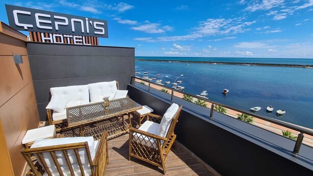 Çepinis Hotel's balcony with wicker furniture, a glass table, and a view of the sea and boats. - Cepnis Hotel (Atakum)