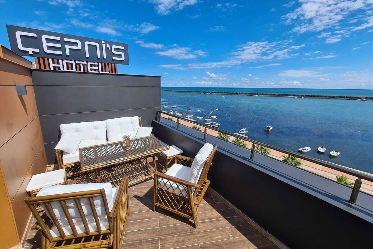 Çepinis Hotel's balcony with wicker furniture, a glass table, and a view of the sea and boats.