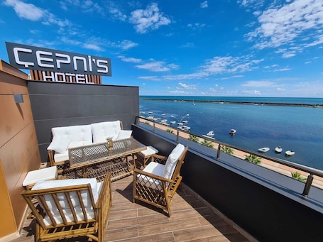 A balcony with wicker furniture, a sign reading 'ÇEPNI'S HOTEL,' and a view of the sea with boats.. Cepnis Hotel