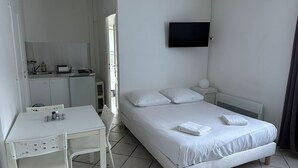 A hotel room with a bed, a desk, a chair, a TV mounted on the wall, and a bathroom visible through an open door. - The countryside 5 minutes from Tours (Fondettes)