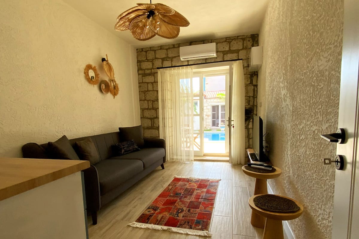 Un espacio habitable pequeño con un sofá, un tapete estampado, una mesa de centro de madera y un ventilador de techo.