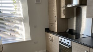 A modern kitchen with light wood cabinets, stainless steel appliances, and a black countertop. - Seaford Sands holiday home with sea view and on South West Coast path (Paignton)