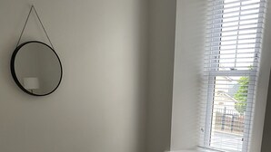 A bedroom with a bed, a round mirror, and a window with blinds. - Seaford Sands holiday home with sea view and on South West Coast path (Paignton)