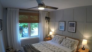 A bedroom with a bed, two bedside tables with lamps, a ceiling fan, a window with curtains, and framed pictures on the wall. - MODERN COTTAGE GETAWAY (Barry's Bay)