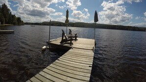 A wooden dock extending into a calm lake with clear skies and a distant forested hill. - MODERN COTTAGE GETAWAY (Barry's Bay)
