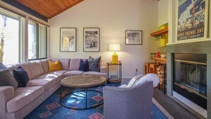 A cozy living room with a wooden ceiling, a fireplace, a sofa, a round coffee table, and a rug.