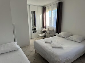 A hotel room with a large bed, two smaller beds, a desk with chairs, and a view of the outdoors through the window. - A Touch of Tenderness in the Heart of the Loire Valley Castles (Fondettes)