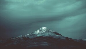 A mountain with a snow-capped peak under a cloudy sky.