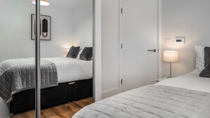 A modern bedroom with a bed, bedside table, lamp, and a wall-mounted thermostat. - Citystay Living - Dutch's Corner (Cambridge)