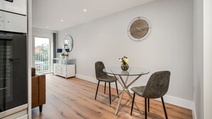 A modern kitchen with a glass dining table and chairs, a round wall clock, and a view of the outdoors through a large window. - Citystay Living - Dutch's Corner (Cambridge)