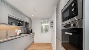 A modern kitchen with grey cabinets, a wooden countertop, a built-in oven, and a window with blinds. - Citystay Living - Dutch's Corner (Cambridge)