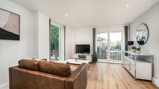 A modern living room with a brown leather sofa, a flat-screen TV, a white coffee table, and a minimalist white cabinet. - Citystay Living - Dutch's Corner (Cambridge)