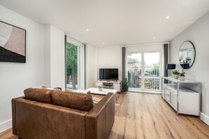 Un salon moderne avec un canapé en cuir marron, un téléviseur à écran plat, une table basse blanche et un meuble blanc au design minimaliste.