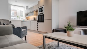 A modern living room with a grey sofa, a coffee table, and a TV. - Citystay Living - Dutch's Corner (Cambridge)