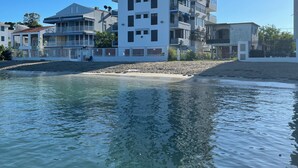 Un edificio moderno de varios pisos con balcones, ubicado cerca de una playa con aguas cristalinas.