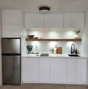 Une cuisine moderne avec des meubles blancs, un réfrigérateur en acier inoxydable, un plan de travail en bois et un robinet noir.