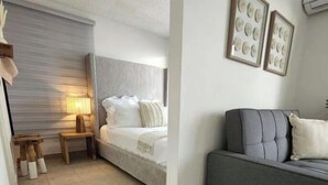 Un dormitorio con cama, mesita de noche, lámpara y un sofá gris.