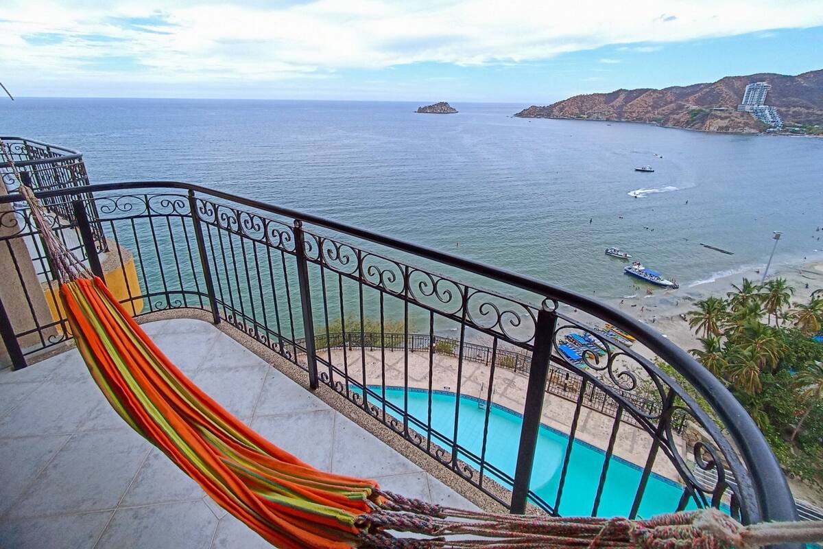 Un balcon avec un hamac, une piscine et une vue sur la mer et la plage.