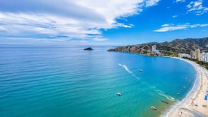 Une vue sur la côte, avec une plage, une eau d’un bleu limpide et une chaîne de montagnes en arrière-plan.
