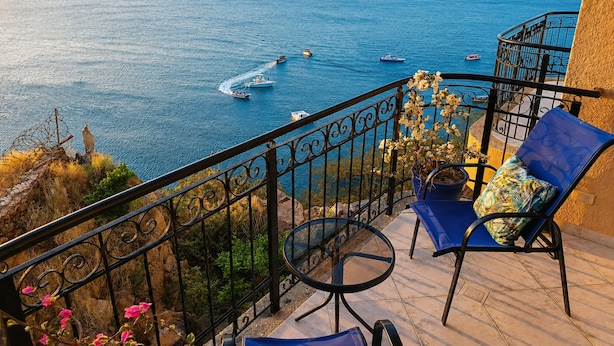 Un balcon avec vue sur la mer, une chaise, un pot de fleurs et une rambarde.