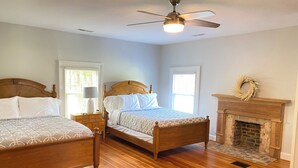 Une chambre à coucher avec deux lits en bois, un ventilateur de plafond, une cheminée et une fenêtre décorée d’une guirlande.
