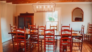 Une salle à manger avec une table et des chaises en bois, un lustre et un grand miroir au mur.