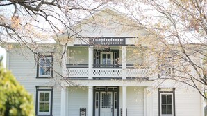 Une maison à deux étages dotée d’un porche à l’avant, d’un balcon et d’une façade symétrique.