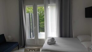 A hotel room with a bed, a small table with a lamp, and a balcony with a view of greenery. - The charm of Touraine (Fondettes)